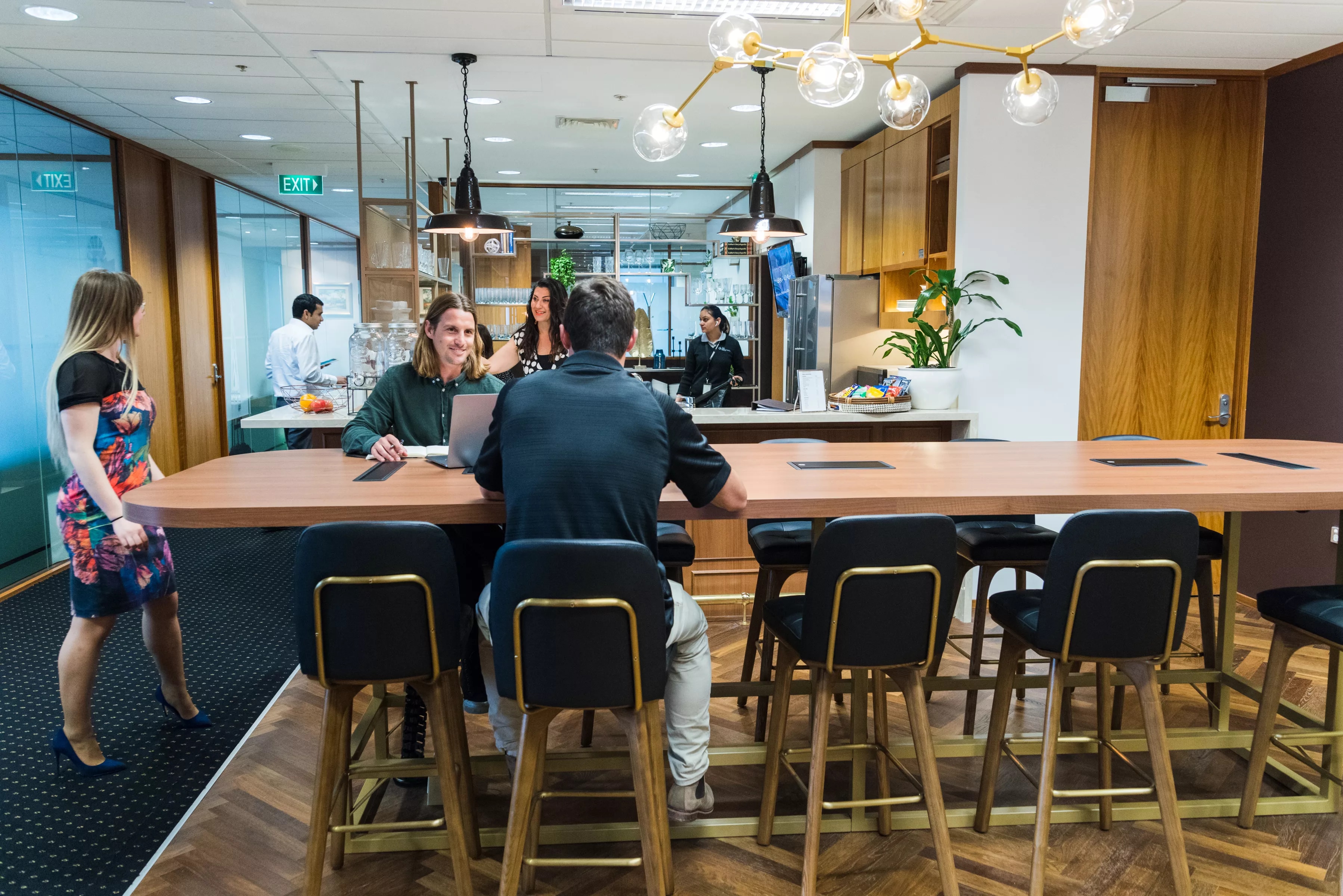 Clients working in a modern coworking space on a large table, enjoying the fully stocked kitchen in Servcorp 140 St Georges Terrace Perth